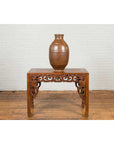 Brown patina Japanese Meiji 19th-century water jar on ornate wooden table, white brick wall background.