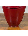 Oxblood ceramic oversized Thai water jar with rope design from Chiang Mai on wood floor against light wall.