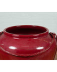 Oxblood ceramic Thai water jar with rope design, oversized, on a light wooden surface.