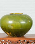 Olive green porcelain circular urn on carved wood base, white background, contemporary Chinese style, close-up view.