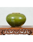 Olive green porcelain urn, circular shape, contemporary Chinese style, on carved floral wooden table.