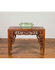 Green celadon ceramic foot bath with handles and foliage motifs on ornate carved wooden table, close-up view.
