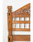 Brown carved wood Indonesian headboard with scrolling foliage and petite baluster details, close-up view.