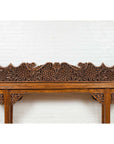 Brown teak carved floral architectural panel on a table in front of a white brick wall.
