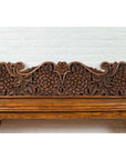 Brown carved teak floral panel set against a white brick wall, antique Indonesian architectural decor.