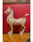 Brown terracotta Han Dynasty horse with short tail on wooden floor against a red wall.