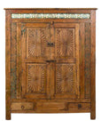 Dark wood Indonesian cabinet with carved sunburst motifs, blue tile accents, two doors, and two small drawers.
