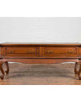 Brown wood Dutch Colonial low table with two drawers and cabriole legs, on wood floor against white brick wall.