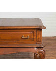 Close-up of a brown wooden Dutch Colonial low table with two drawers and cabriole legs on a wooden floor.