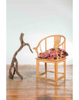 Brown Indonesian river wood sculpture next to a wooden chair with patterned cushions on a wooden floor.