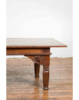 Dark wood Indonesian Madurese coffee table with carved spandrels on wooden floor against a white wall.