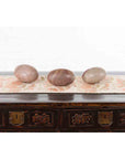 Close-up of three two-toned Shiva Lingam stones from Narmada River on patterned cloth and carved wooden table.