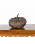 Bronze pumpkin sculpture with rustic patina on a wooden table, white background, close-up.