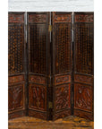 Brown and red lacquered eight-panel Chinese screen with gilt motifs and gold calligraphy, set against a brick wall.
