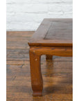 Close-up of a two-toned wood Chinese vintage low coffee table with curved legs on a worn wooden floor.