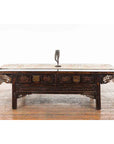 Dark wood antique table with ornate carvings and brass handles, vintage bronze ballerina leg candle holder on wood floor.