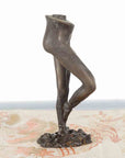 Bronze ballerina leg candle holder in battement frappé position on patterned surface, vintage style, close-up.