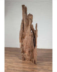 Brown driftwood carving from Northern Thailand on wooden base, placed in front of a white brick wall.