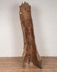 Brown driftwood carving, wood material, displayed on wooden floor with white brick wall in background, indoor setting.