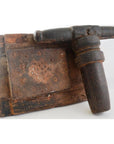 Close-up of a vintage hand-sculpted metal Animal Noodle Maker on a weathered, holey wooden board.