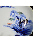 Close-up of blue and orange hand painted porcelain bowl with landscape, tree, and distant buildings design, antique Asian style.