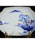 Blue and orange hand painted porcelain bowl with mountain, tree, and water landscape on display stand.