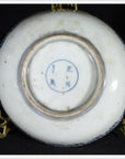 Close-up of the underside of a white porcelain bowl with blue markings, resting on a gold stand.