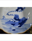 White porcelain bowl with hand painted house, trees, sailboat by water, and gold rim accents, close-up.