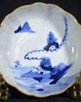 Close-up of blue and white hand painted porcelain bowl with mountain landscape motifs on ornate gold stand.