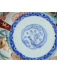 Close-up of antique Asian porcelain bowl base with blue circle and red, green, gold hand-painted floral accents.