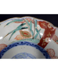 Close-up of antique Asian porcelain bowl with vibrant red, blue, and green hand-painted floral patterns.