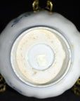 Close-up of the underside of an antique hand painted Asian porcelain bowl with a small square sticker on metal stand.