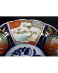 Close-up of a red, green, gold, and blue hand painted porcelain bowl with floral and landscape designs.
