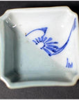 Close-up of blue and white hand-painted porcelain dish with abstract design, displayed on a dark modern surface.