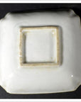 White porcelain dish, hand-painted, shown upside down with unglazed recessed base on dark background, close-up.