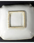White porcelain dish, hand-painted, shown upside down with unglazed recessed base on dark background, close-up.