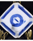 Blue and white hand painted porcelain dish with central symbol, displayed on a brass stand.