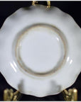 White and multicolor hand painted porcelain dish with scalloped edge on gold stand, dark background.