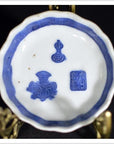 Blue and white porcelain dish, hand painted with Asian design, displayed on brass stand against dark background.