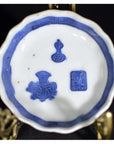 Blue and white porcelain dish, hand painted with Asian design, displayed on brass stand against dark background.