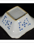 Close-up of an antique Asian porcelain dish with blue dotted sides on a black background.