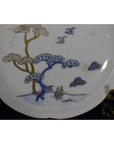 White porcelain plate with hand-painted birds, twin pine trees, and abstract cloud patterns, close-up view.