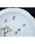 White porcelain plate with gold rim, hand painted soaring birds and twin pine trees, antique Asian design, close-up.