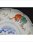 White porcelain plate with hand-painted prancing goats and stylized plants, antique Asian design, close-up view.