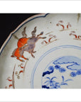 Blue and white porcelain plate with hand-painted prancing goats and floral rim pattern, close-up view.