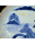Close-up of antique Asian porcelain plate with hand painted misty peaks, arched bridge, and gold-trimmed edge.