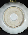 Close-up of the underside of a white porcelain plate with a round foot ring on a gold stand.
