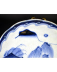 Close-up of blue and white hand painted porcelain plate with river pavilion and willow grove, wavy patterned border.