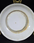 Close-up of an antique hand painted porcelain plate with visible wear on underside, displayed on a gold stand.