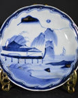 White porcelain plate with hand-painted River Pavilion, willow trees, mountains, and sailboat motifs, close-up view.